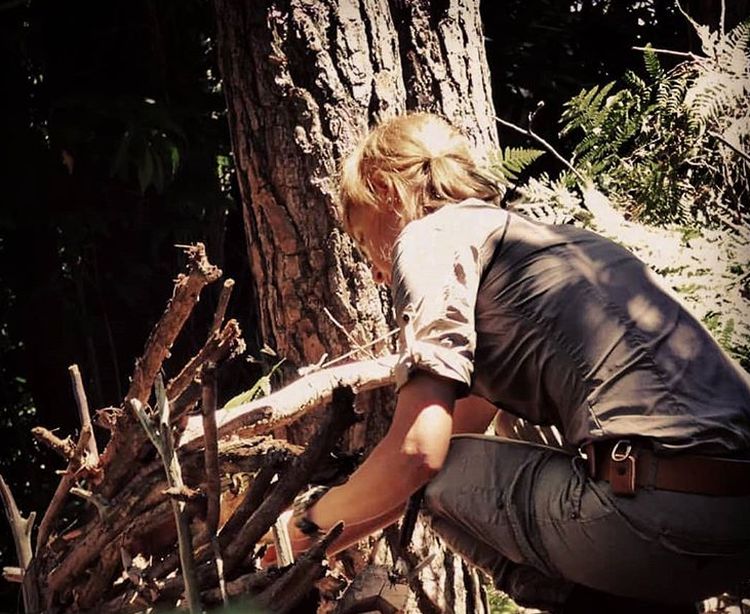 Woman finalizing a hidden bushcraft shelter